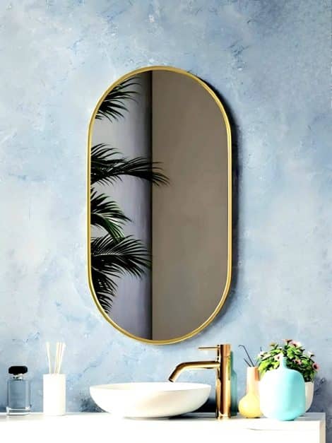 Above a sink, a round mirror with an aluminum frame reflects a nearby plant, enhancing the space's aesthetic. Capsule Framed Mirror.