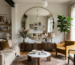 Living room with beige sofa, mustard armchair, round mirror, coffee table, and large window with garden view